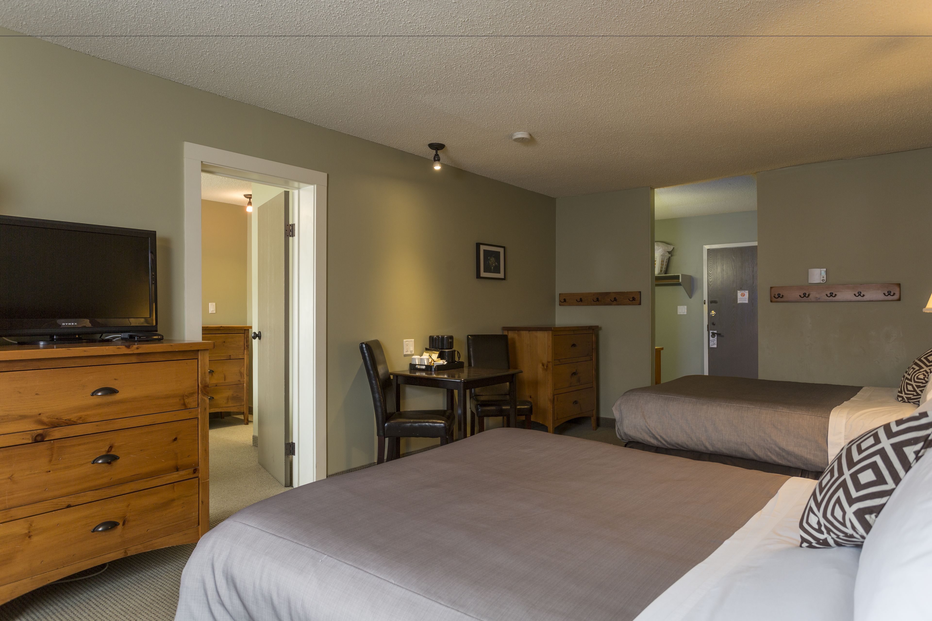 A hotel room with two beds, a wooden dresser, a desk with a chair, and a television on the dresser.