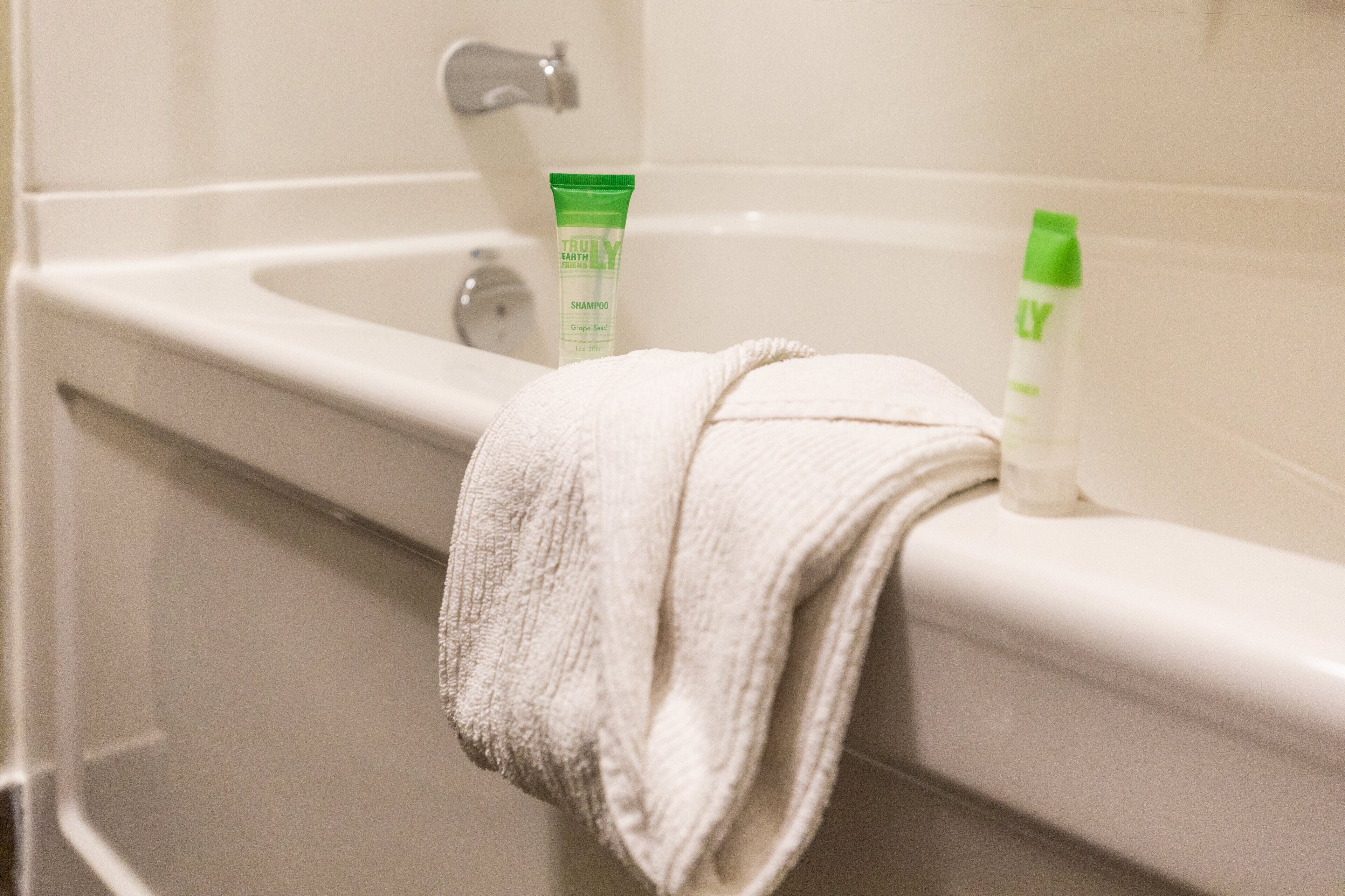 A bathroom with a bathtub, a towel, and two bottles of shampoo.