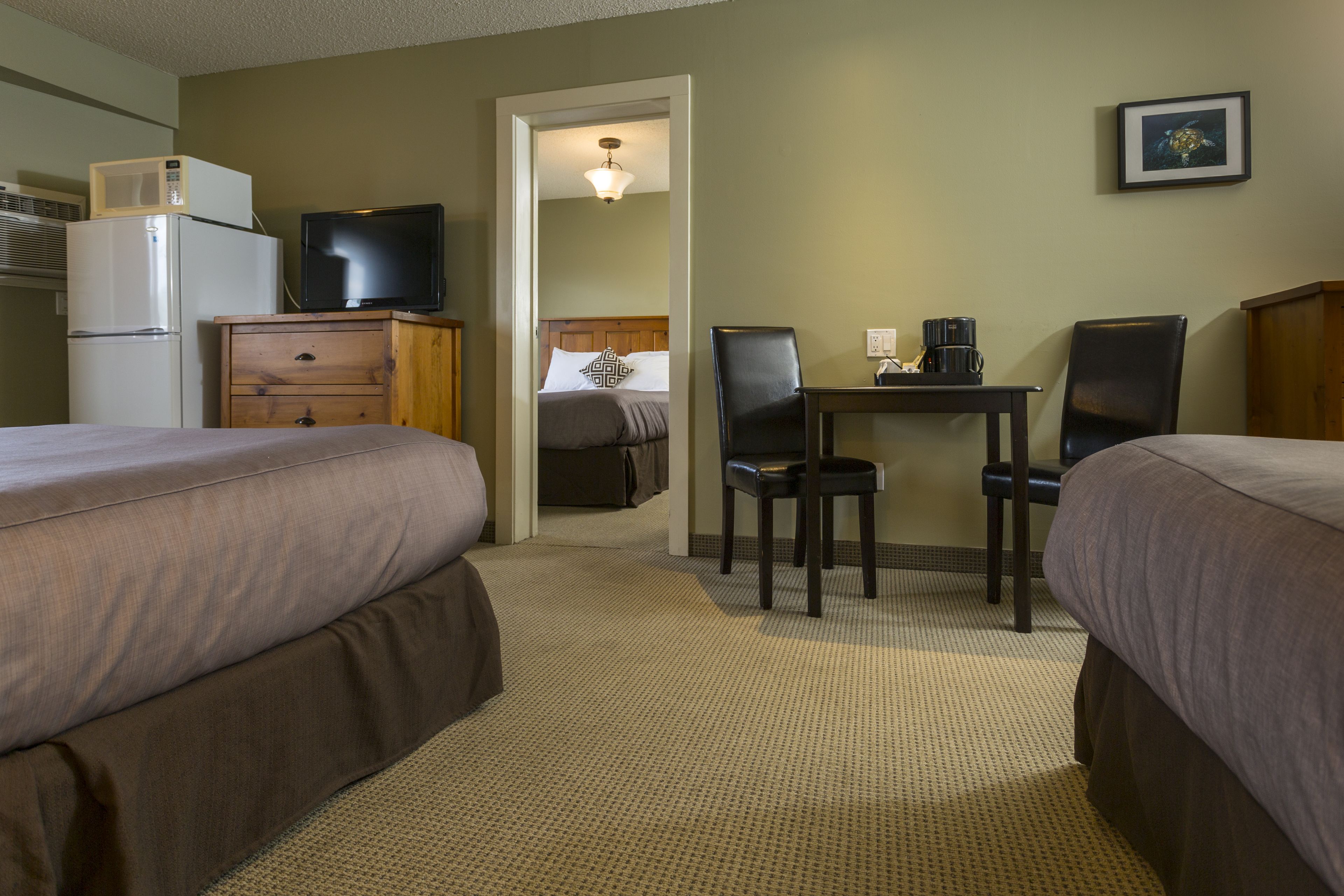 A hotel room with two beds, a desk with a chair, a television, a microwave, and a refrigerator.