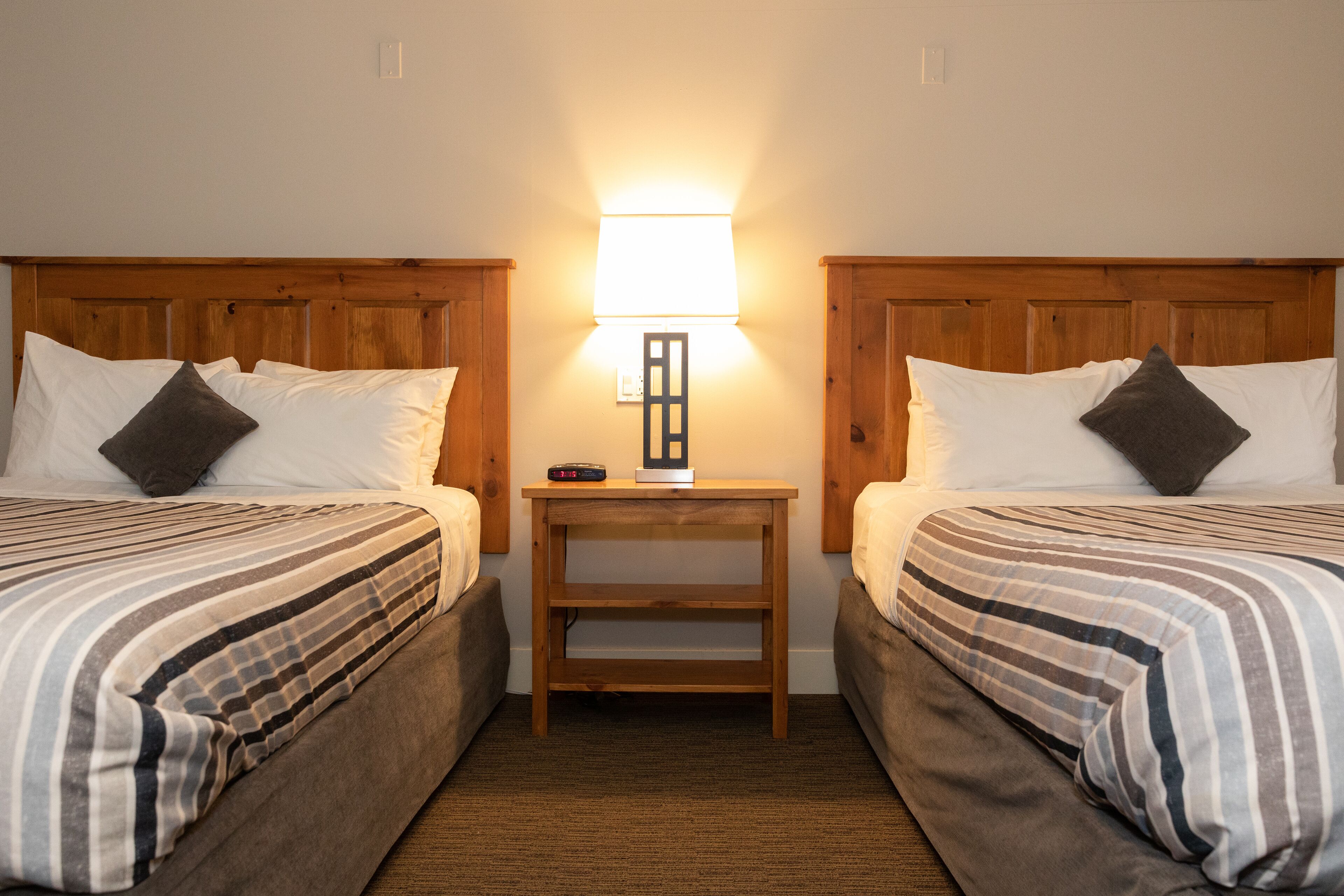 Une chambre d’hôtel avec deux lits, une table de chevet avec une lampe et une petite table.