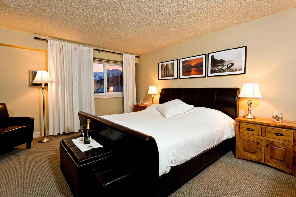 Habitación de hotel con cama, mesitas de noche, escritorio, silla y ventana con cortinas.