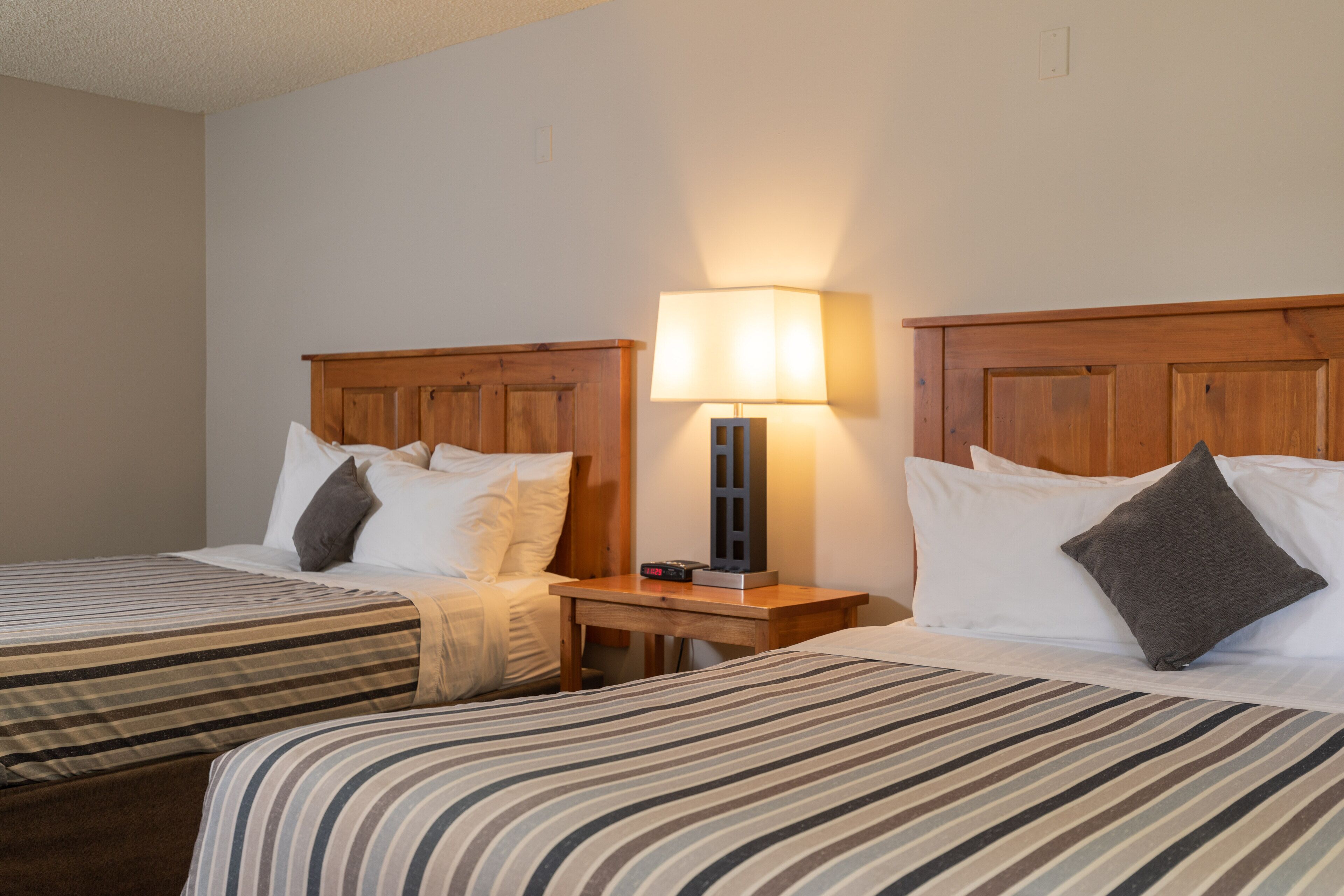 A hotel room with two beds, a nightstand with a lamp, and a wooden headboard.