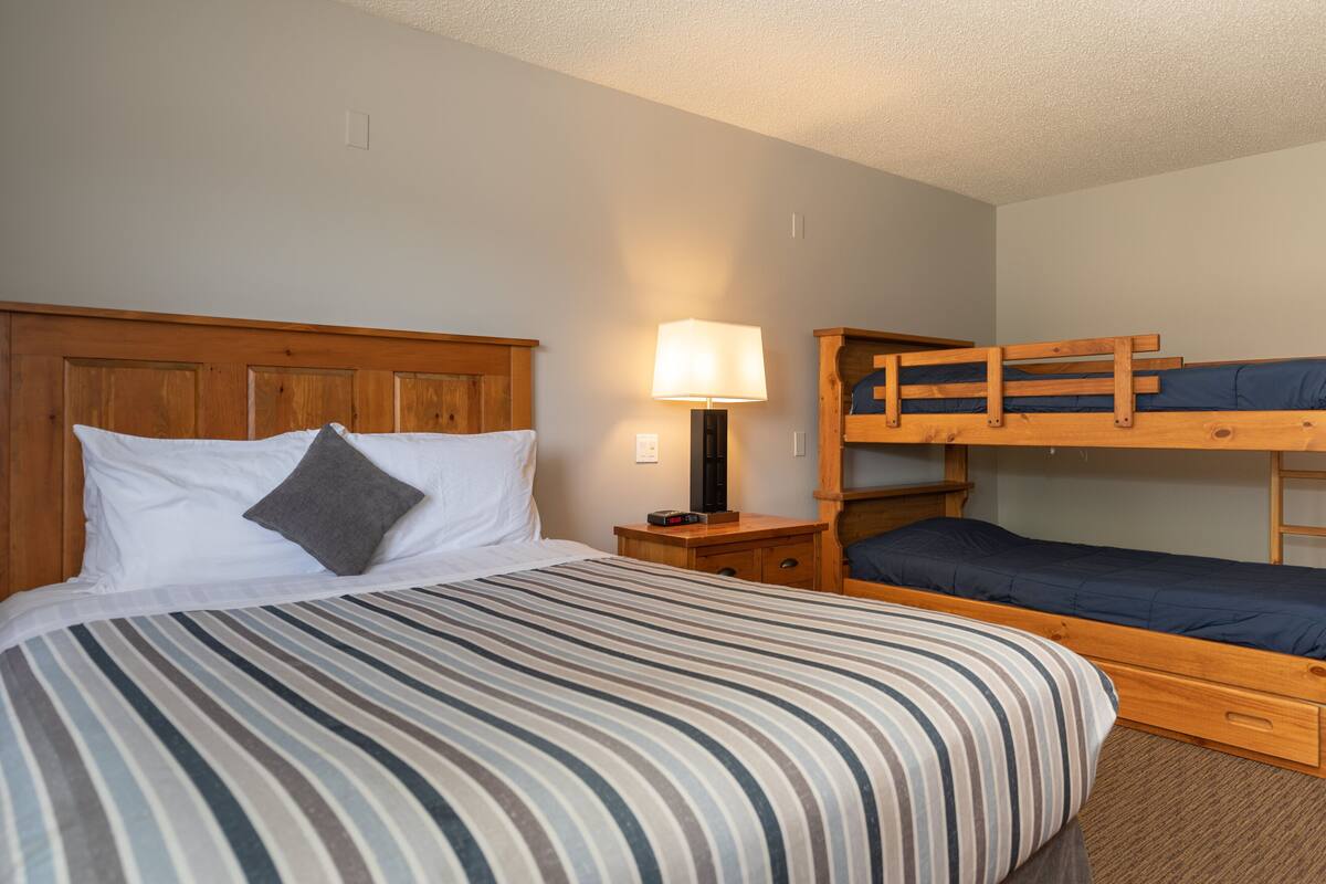 Una habitación con una cama individual, una mesita de noche, una lámpara y una cama litera.