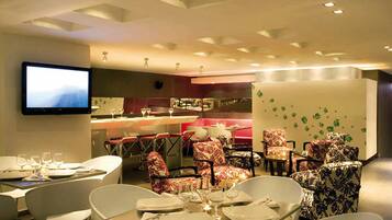 A modern dining area with tables set for two, a bar area, and a television mounted on the wall.