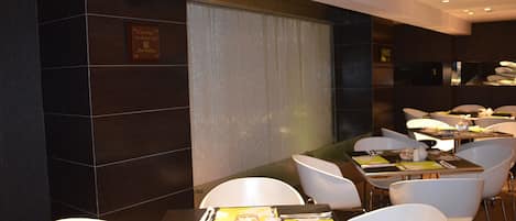 A modern dining area with tables set for two, white chairs, and a large window with curtains.