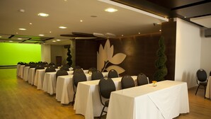 Un salón de conferencias con filas de mesas y sillas, una pantalla verde y una pared decorativa.