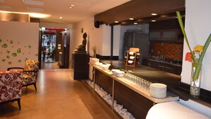 Un vestíbulo de hotel con recepción, zona de estar y vistas a la cocina.