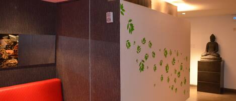 A modern lobby with a red sofa, a wall with green leaf decals, and a Buddha statue.