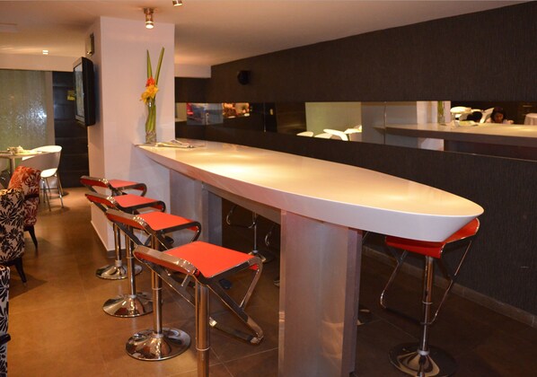 Un área de bar moderna con una barra larga y cuatro taburetes rojos.
