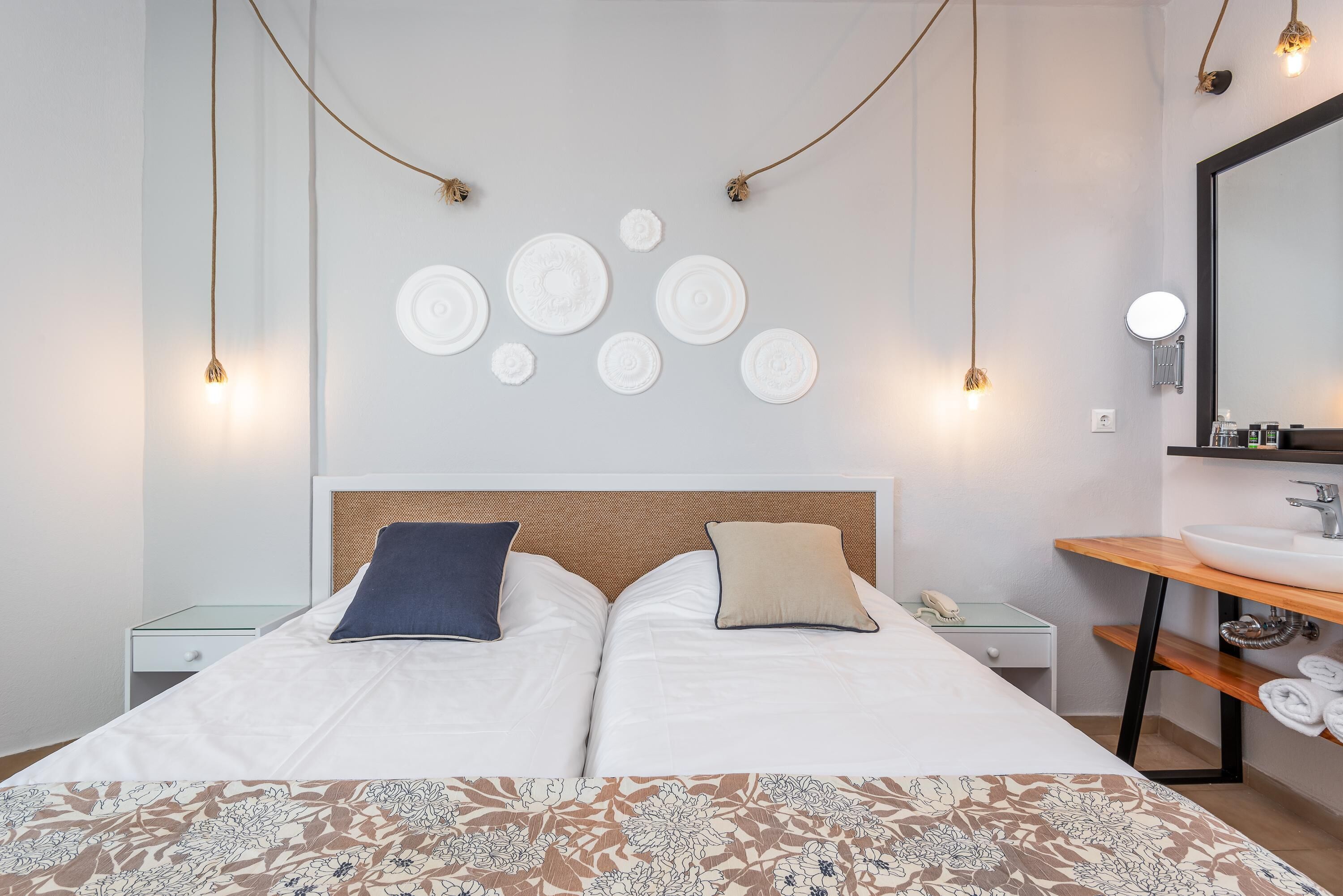 Cama doble con dos almohadas, mesita de noche, espejo, estante de madera con toallas y decoración en la pared.