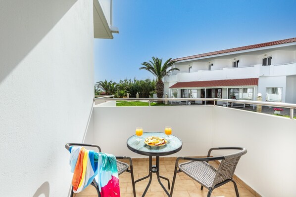 A balcony with a table set for two, two glasses of orange juice, and a plate of food. - Mrs Chryssana Beach Hotel by GHH (Platanias)