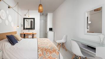 Une chambre moderne avec un lit, un bureau et une chaise, une salle de bain à l’arrière-plan et un luminaire suspendu.