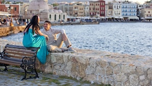 A couple sitting on a stone wall by a waterfront with a cityscape in the background. - Mrs Chryssana Beach Hotel by GHH (Platanias)