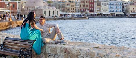 A couple sitting on a stone wall by a waterfront with a cityscape in the background.