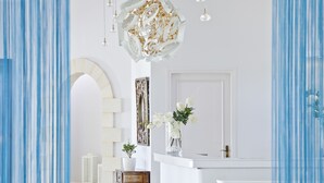 A modern interior with a white reception desk, a decorative chandelier, and a vase with white flowers. - Mrs Chryssana Beach Hotel by GHH (Platanias)