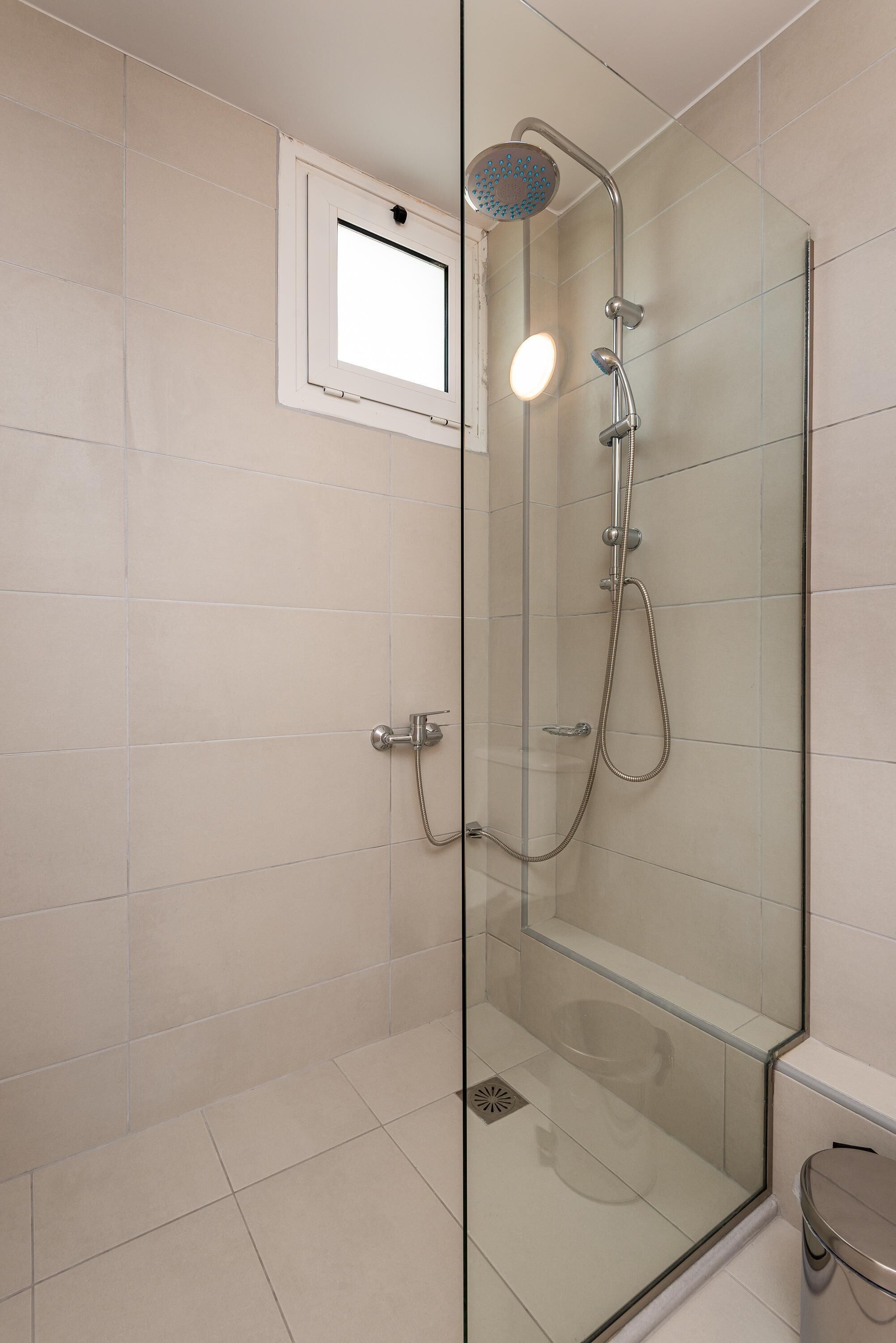 Une douche moderne dotée d’une paroi en verre, d’un pommeau de douche à main et d’un panneau de commande fixé au mur.