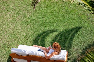 A person lying on a sunbed in a grassy area with a white cushion and a smartphone.