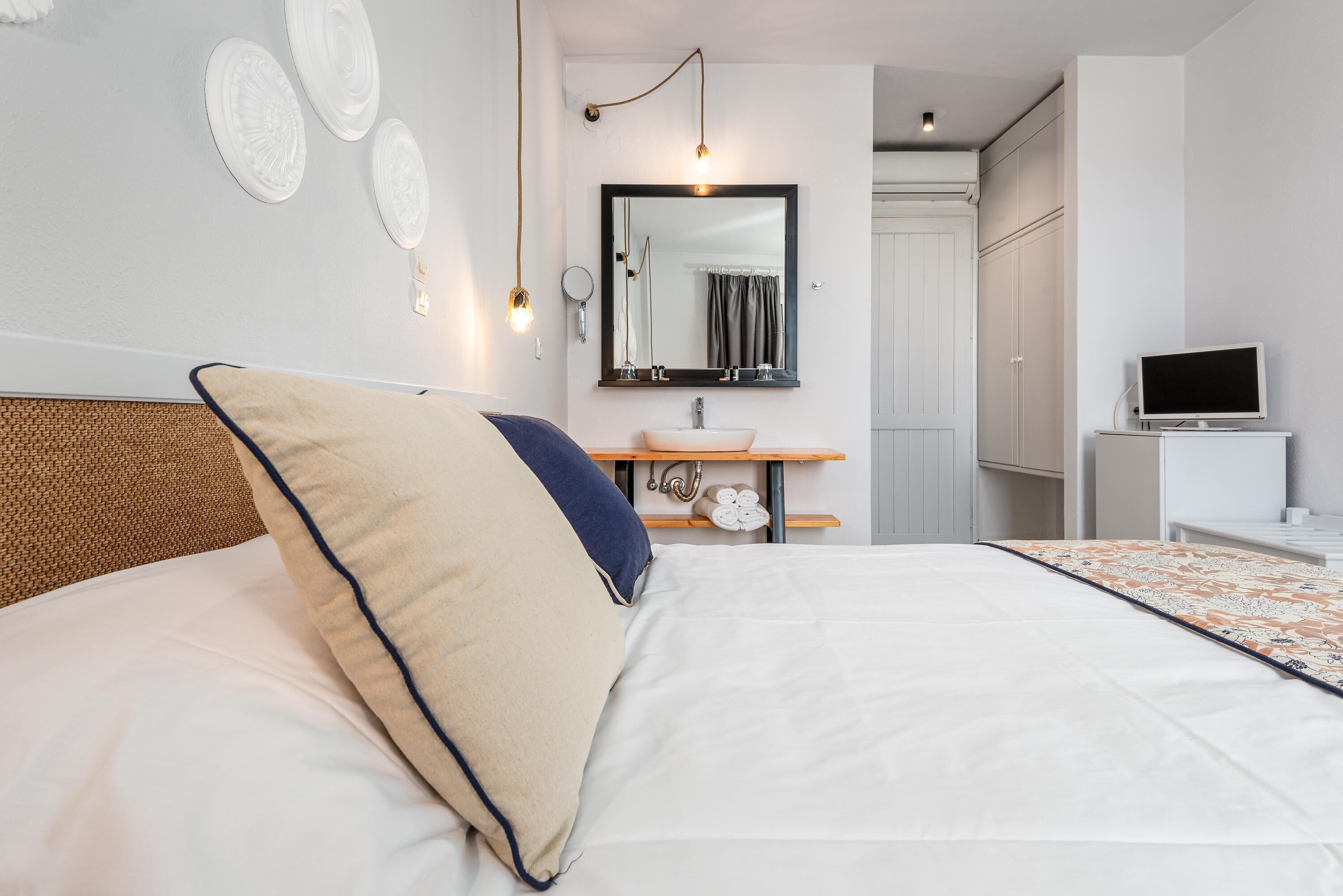 Un dormitorio ordenado con cama, mesita de noche, espejo, lavabo y televisor.