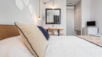 Un dormitorio ordenado con cama, mesita de noche, espejo, lavabo y televisor.