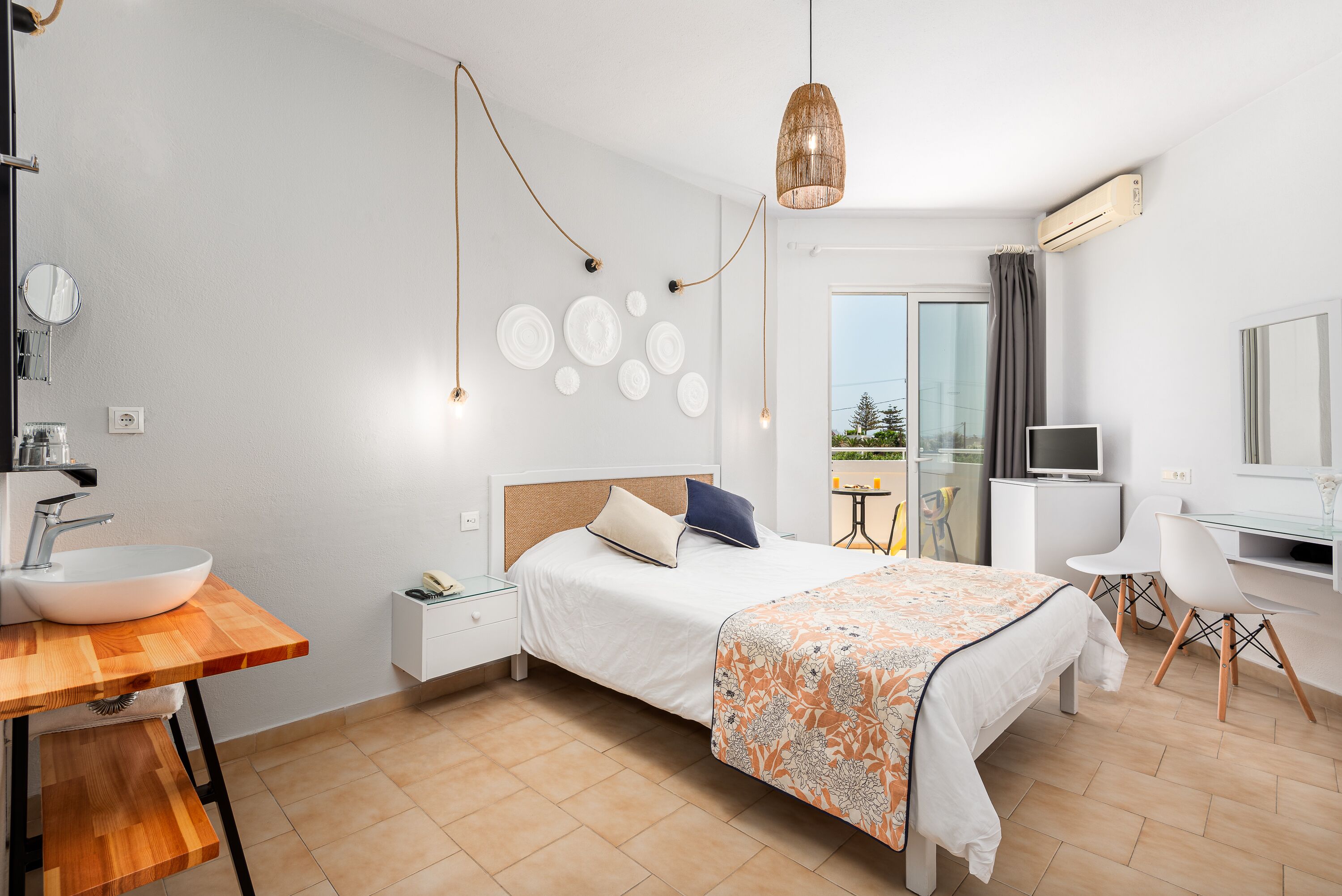 A modern hotel room with a large bed, a wooden desk with a sink, a TV, and a balcony with a view.