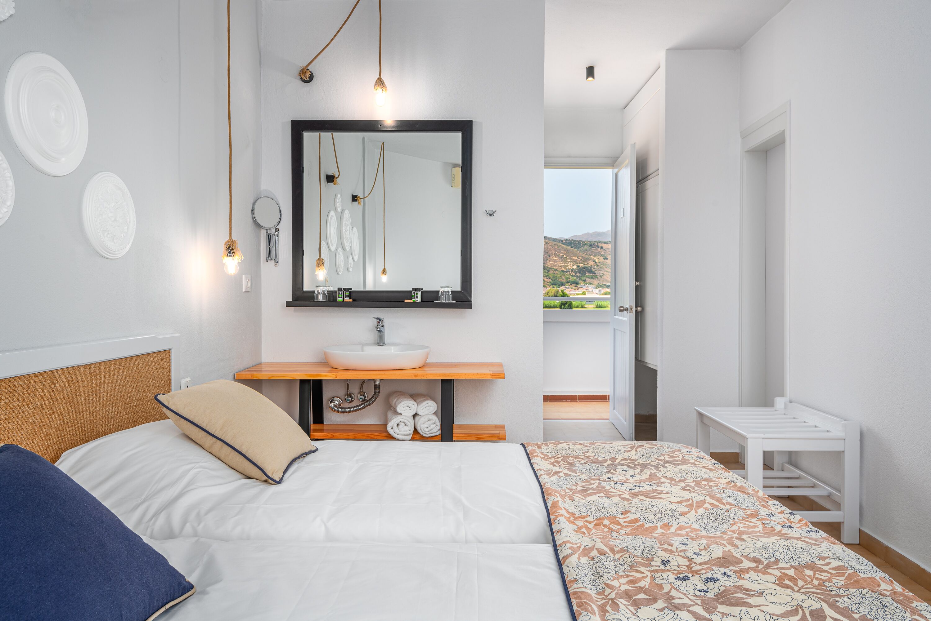 A modern bedroom with a bed, a bedside table, a mirror, a sink, and a view of the outdoors.