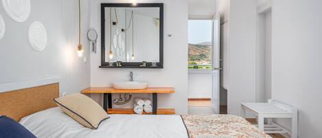 A modern bedroom with a bed, a bedside table, a mirror, a sink, and a view of the outdoors.