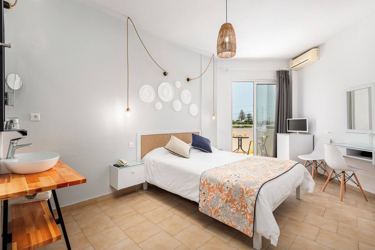Una habitación de hotel moderna con una cama grande, un escritorio de madera con un lavamanos, un televisor y un balcón con vistas.
