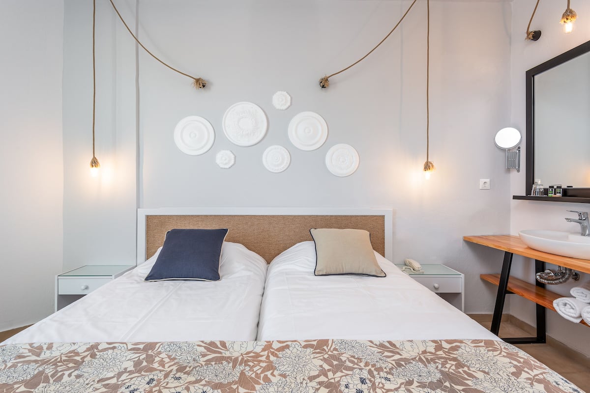 Una cama doble con una colcha estampada, dos almohadas, una mesita de noche con un teléfono y un espejo fijado a la pared.