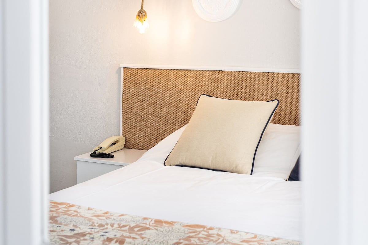 Una habitación de hotel ordenada con una cama, una mesita de noche con teléfono y una lámpara colgante.