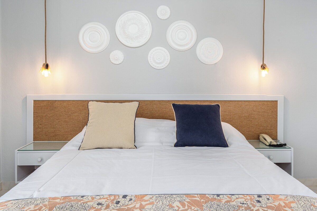 A neatly made bed with a patterned bedspread, two bedside tables with lamps, and decorative wall plates.