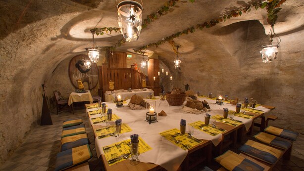 A long dining table set with candles, benches, and a rustic stone wall background.