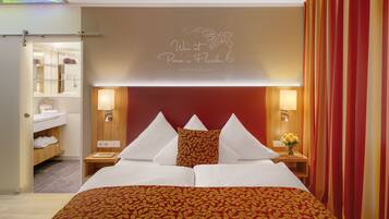 A hotel room with a red and gold patterned bedspread, a wooden headboard, and a wall-mounted light fixture.