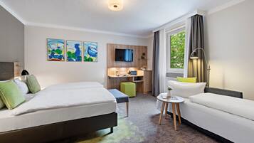Ein Hotelzimmer mit zwei Betten, einem Schreibtisch, einem Fernseher und einem Fenster mit Vorhängen.