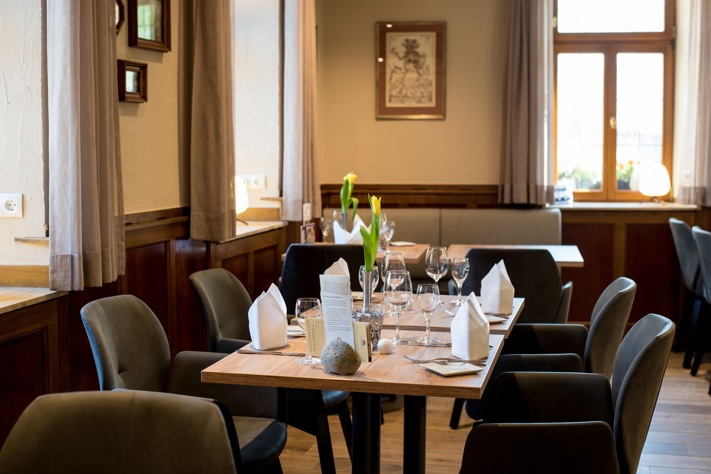 Un restaurant avec une table en bois dressée pour un repas, des chaises et un vase rempli de fleurs.