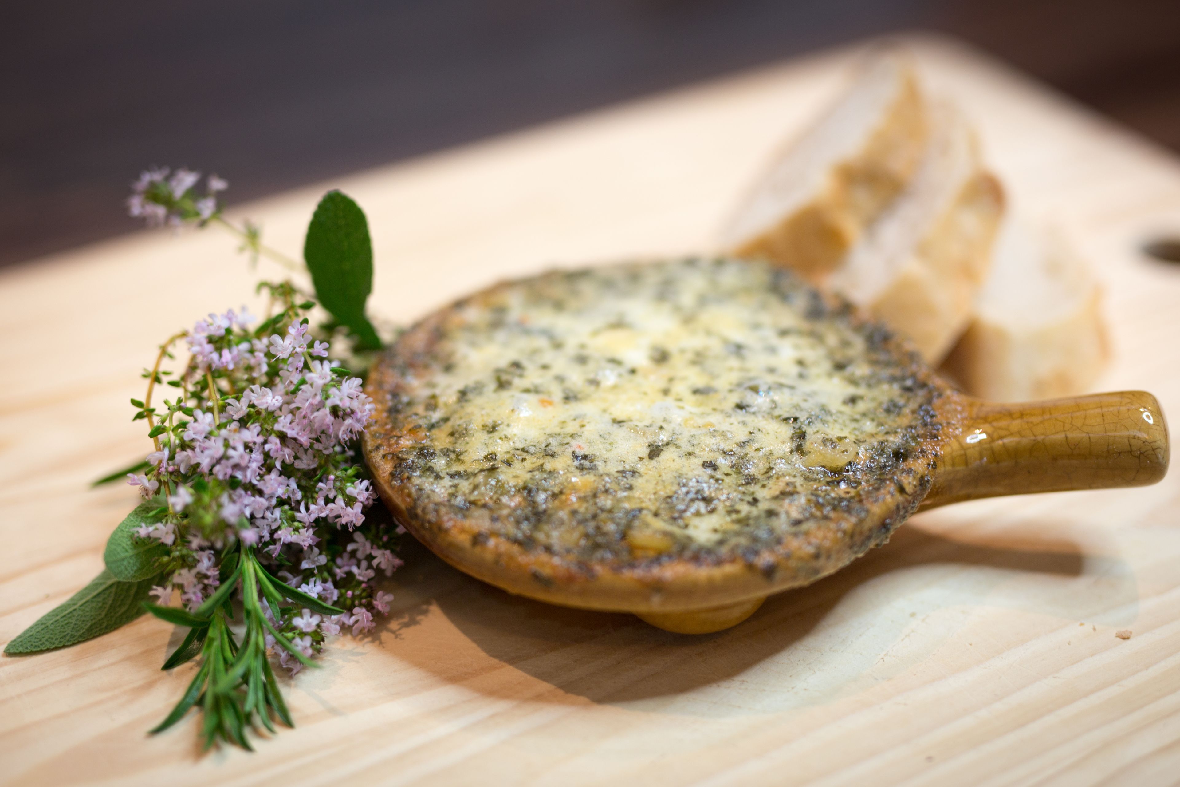 A cheese board with a cheese dish, bread, and herbs.