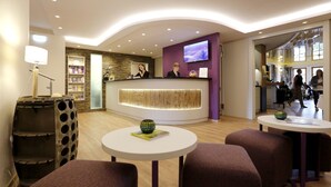 A modern reception area with a curved reception desk, a television mounted on the wall, and a seating area with round tables and cushioned chairs.