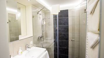 Un baño moderno con ducha de vidrio, un lavabo blanco y un espejo grande.