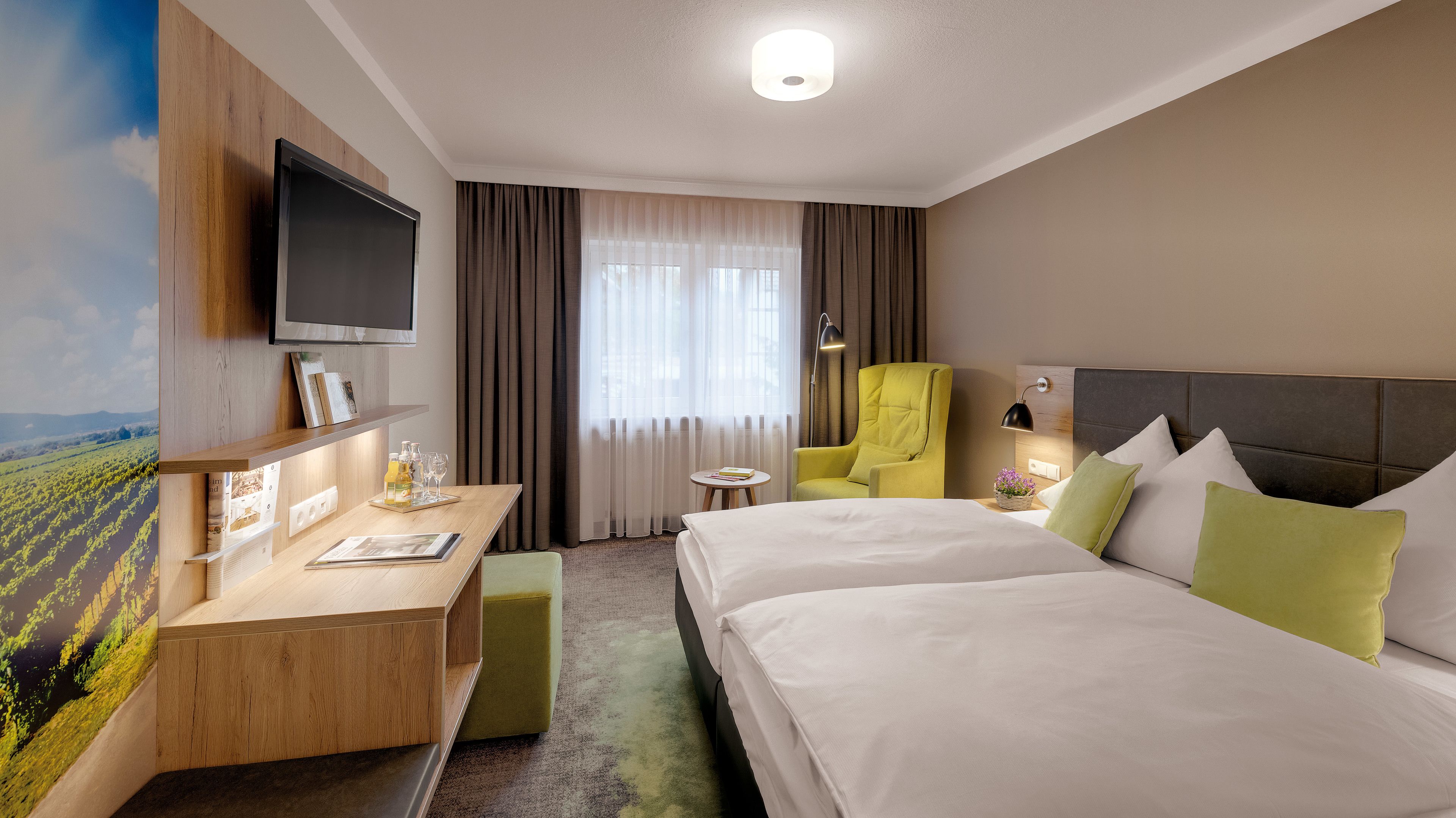 Een hotelkamer met een bed, een bureau, een stoel, een televisie en een raam met gordijnen.