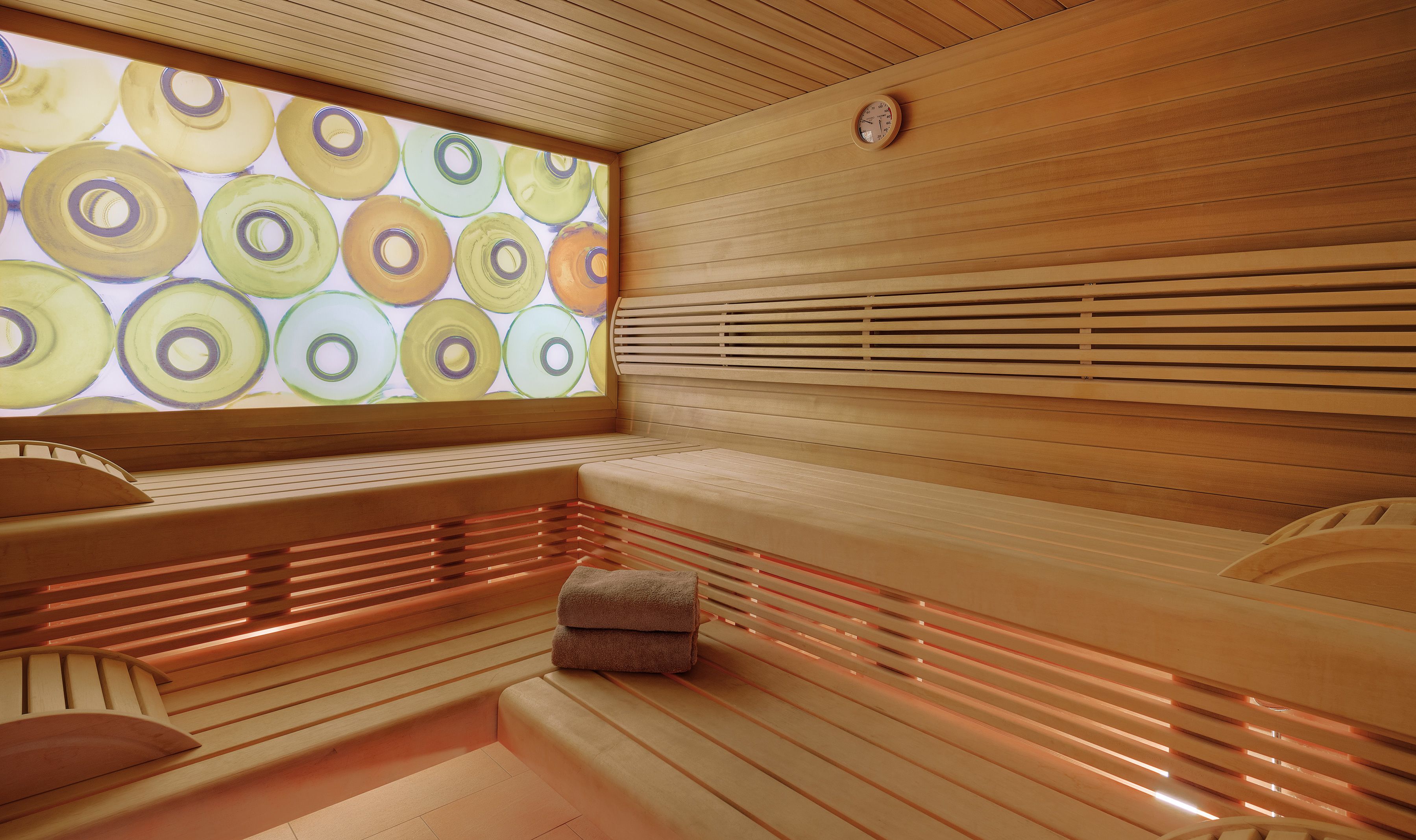 Eine Sauna mit Holzbänken, einer Wanduhr und einem farbenfrohen, kreisförmigen Muster an der Wand.