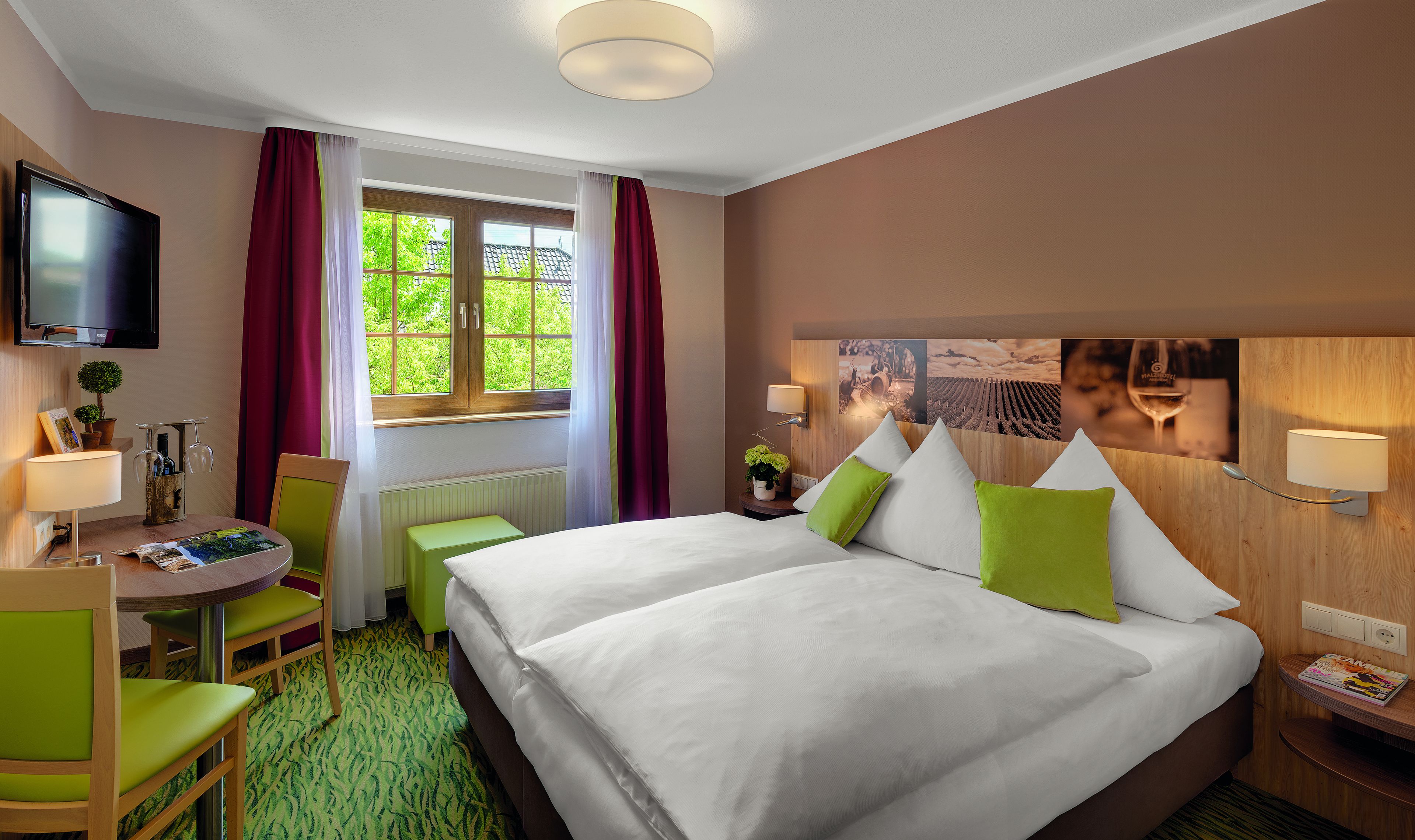 A hotel room with a bed, a desk, a chair, a TV, and a window with curtains.