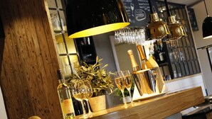 A bar area with a wooden counter, bottles, glasses, and a decorative plant.