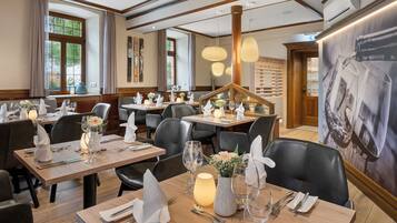 Un restaurant avec des tables en bois, des chaises en cuir noir et des centres de table éclairés par des bougies.
