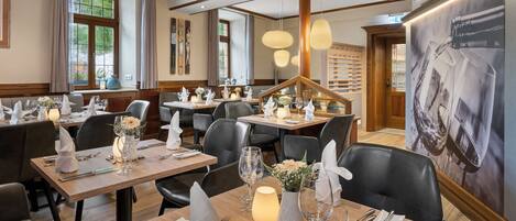 Un restaurant avec des tables en bois, des chaises en cuir noir et des centres de table éclairés par des bougies.