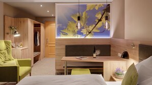 A modern hotel room with a bed, a desk with a chair, a wardrobe, and a large window with a leaf design.
