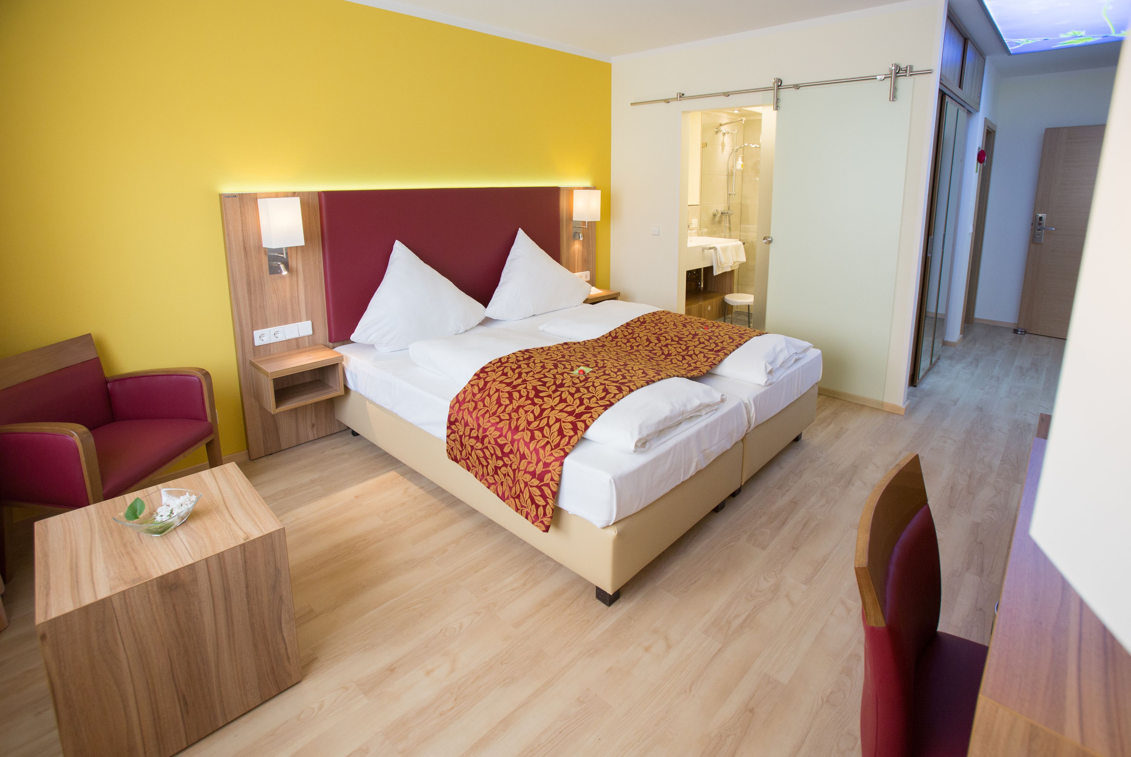 A hotel room with a bed, a nightstand, a desk, a chair, and a bathroom visible through an open door.