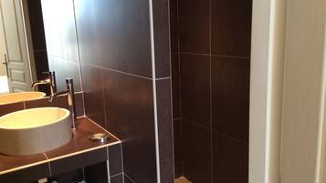 Un baño moderno con baldosas oscuras, un lavabo redondo y una zona de ducha.