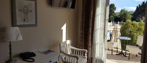 A room with a desk, a chair, a television, and a view of the outdoors.