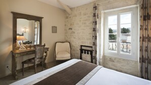 A bedroom with a bed, a desk with a chair, a mirror, and a window with a view. - Hôtel Le Mas Saint-Joseph (St.-Rémy-de-Provence)