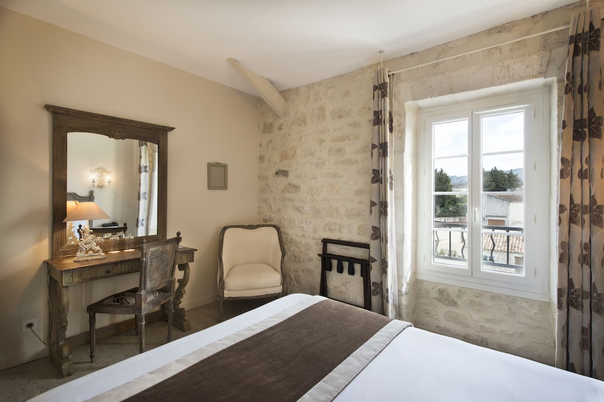 Une chambre à coucher avec un lit, un bureau et une chaise, un miroir et une fenêtre donnant sur un paysage agréable.