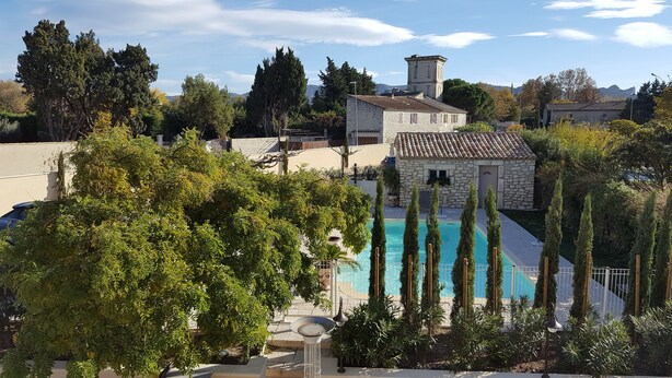 A stone building with a swimming pool surrounded by tall trees and a clear sky. - Hôtel Le Mas Saint-Joseph (St.-Rémy-de-Provence)